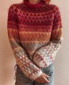 a woman wearing a multicolored sweater standing in front of a wall with her hands on her hips