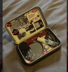 an open tin box with various items inside on a bed