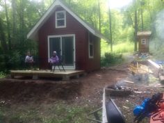 two people sitting on the porch of a small red cabin in the middle of a wooded area