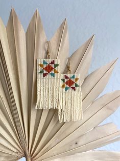 a pair of earrings hanging from a wooden fan shaped object on top of a table