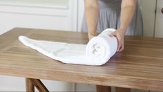 a woman is rolling up a white towel on top of a wooden table