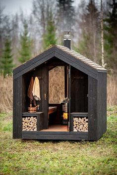 an outhouse with logs in the front and side doors open on top of grass