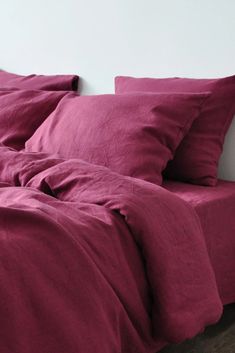 an unmade bed with red sheets and pillows on top of it, in front of a white wall