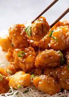 the chicken is being served with chopsticks on top of white rice and garnished with sesame seeds