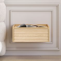 an open book sitting on top of a wooden box next to a white chair and wall