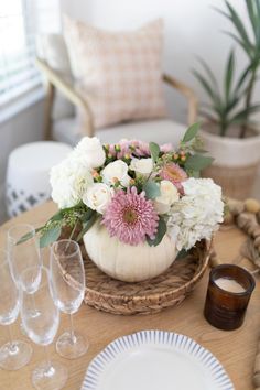 the table is set with white and pink flowers in a pumpkin - shaped vase on top of a wicker basket