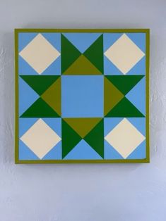 a blue and green square with white squares in the middle is hanging on a wall