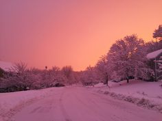 the sun is setting over a snow covered road in front of a house and trees