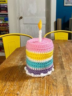 a multicolored cake sitting on top of a wooden table next to yellow chairs