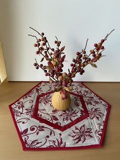 a vase filled with flowers sitting on top of a red and white table cloth covered placemat