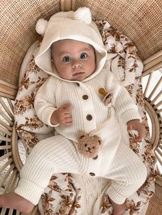 a baby in a white bear suit is laying on a wicker chair with a teddy bear