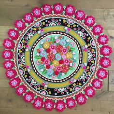 a crocheted doily with flowers and leaves in the center on a wooden floor