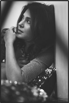 a black and white photo of a woman leaning against a wall with her hand on her chin