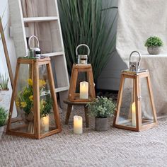 three wooden lanterns with lit candles in them on the ground next to potted plants