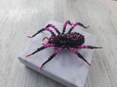 a beaded spider sitting on top of a white marble block with pink and black beads