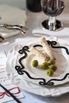 a white plate topped with crackers and green olives next to a glass of wine