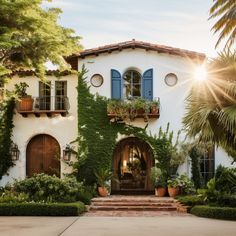 a white house with blue shutters and green plants on the front door, surrounded by greenery