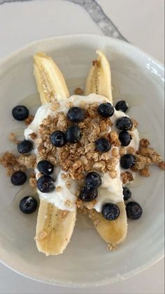 a white plate topped with bananas and blueberries covered in yogurt next to granola