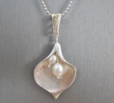 A lovely Calla Lily pendant in brushed silver has double lustrous white Freshwater pearls in its center. It hangs simply from a delicate silver ball chain. Length measures 16 inches but can easily be adjusted upon request.  A perfect necklace for bridesmaids or bridal parties!  Pendant measures almost 1 1/2 inches in length and 1 inch in width. Delicate Silver Drop Necklace For Anniversary, Silver Drop Necklace With Pearl Pendant For Anniversary, Wedding Pearl Necklace With Flower Pendant, Sterling Silver Drop Necklace With Pearl Pendant For Wedding, Wedding Pearl Drop Flower Pendant Necklaces, Silver Pearl Wedding Necklace With Flower Pendant, Wedding Pearl Drop Flower Pendant Necklace, Delicate Silver Teardrop Pearl Necklace, Silver Teardrop Pearl Necklace For Anniversary