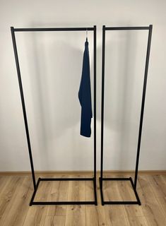 two black clothes racks with blue towels hanging from them on wooden floors in front of a white wall