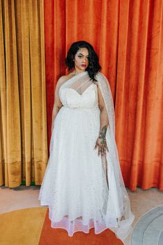 a woman in a white dress and veil posing for the camera with an orange curtain behind her