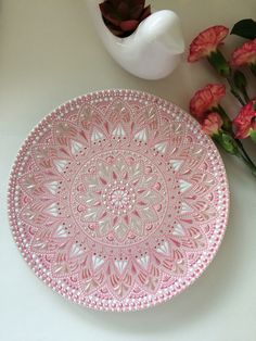 a pink plate sitting on top of a table next to flowers and a white vase