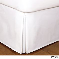 a white bed skirt on top of a wooden floor