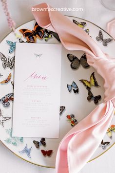 a white plate topped with butterflies next to a pink napkin on top of a table