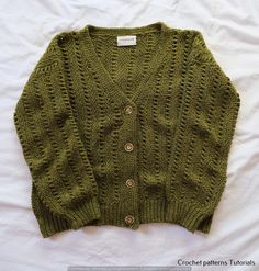 a green knitted sweater laying on top of a bed