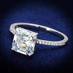 an engagement ring with a square cut diamond surrounded by pave diamonds on a blue velvet surface