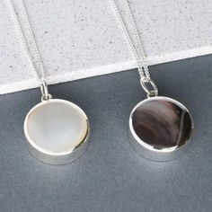 two pendants on a gray surface one has a white shell and the other is black