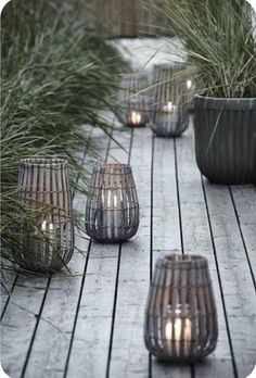 several lit candles are sitting on a wooden deck next to some plants and grass in pots