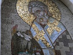 the mosaic on the side of a building has a man holding a cross in his hand