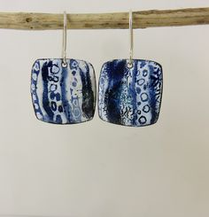 two square shaped blue and white ceramic earrings hanging from a wooden hook on a twig