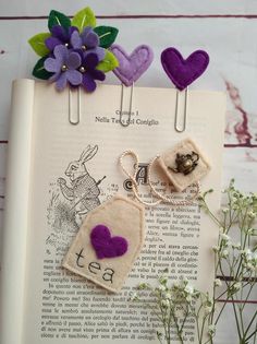 two bookmarks with purple hearts on them sitting on top of an open book next to flowers