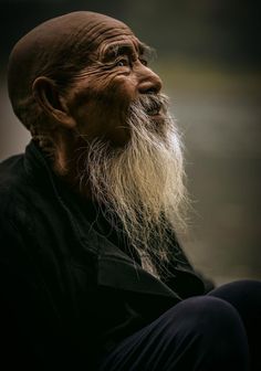 an old man with long white beard and black shirt sitting on the ground in front of him