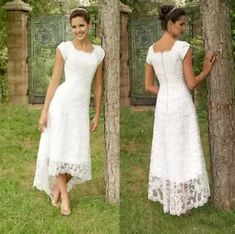 a woman in a white dress standing next to a tree