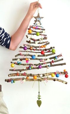 a person holding up a christmas tree made out of branches with ornaments hanging from it