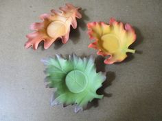 three plastic leaves are sitting on a table top, one is green and the other is yellow