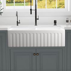 a white sink sitting under a window next to a kitchen faucet and cabinets