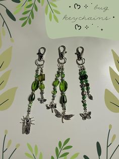 four charms are hanging on a wall with leaves and flowers in the background, one is green