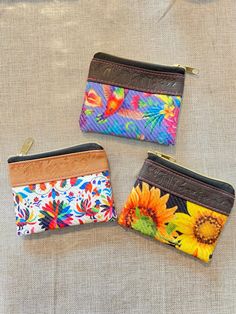 three small wallets with flowers on them sitting on a cloth covered surface, one has a zippered closure and the other has an embellishment