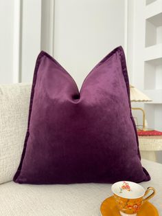 a purple pillow sitting on top of a couch next to a cup and saucer