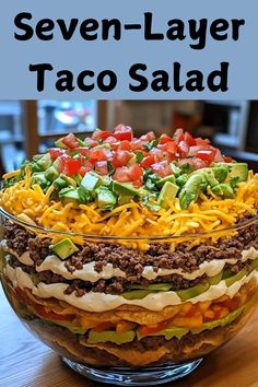 seven layer taco salad in a glass bowl on top of a wooden table with text overlay that reads seven layer taco salad