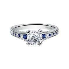 a white gold engagement ring with blue sapphire stones on the sides and an engraved band