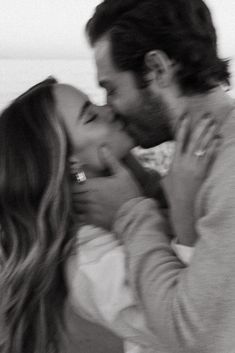 a man and woman kissing each other on the beach in front of the ocean, black and white photo