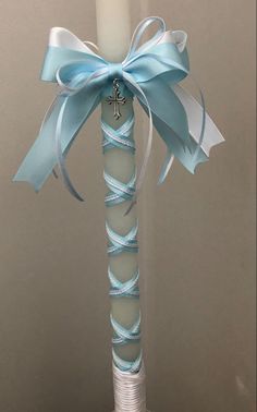 a white candle with a blue ribbon tied around it and a cross on the top