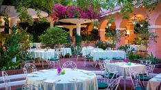 an outdoor restaurant with tables and chairs covered in white tablecloths surrounded by greenery