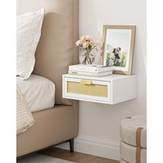 a white nightstand with flowers on it next to a bed and a framed photo in the corner