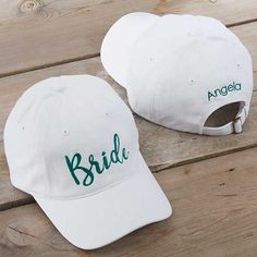 two white hats with green bride and groom embroidered on them sitting on a wooden surface